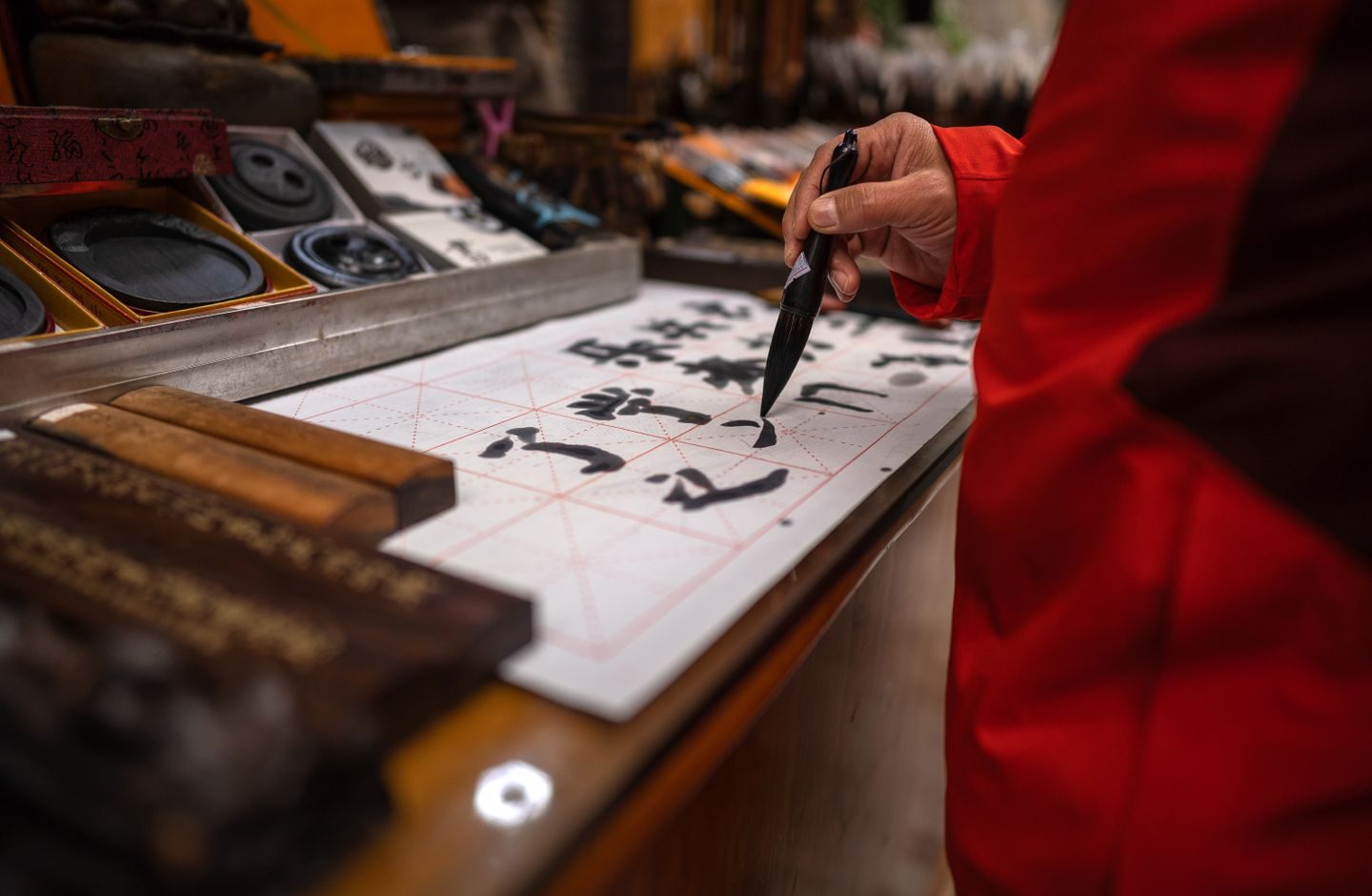 A person practicing Chinese brush calligraphy on paper marked with a guide grid.