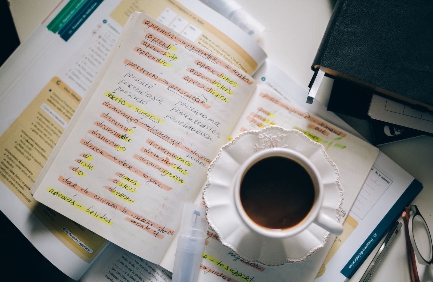 A cup of coffee next to an open notebook covered in handwritten language-learning notes and highlighted vocabulary.