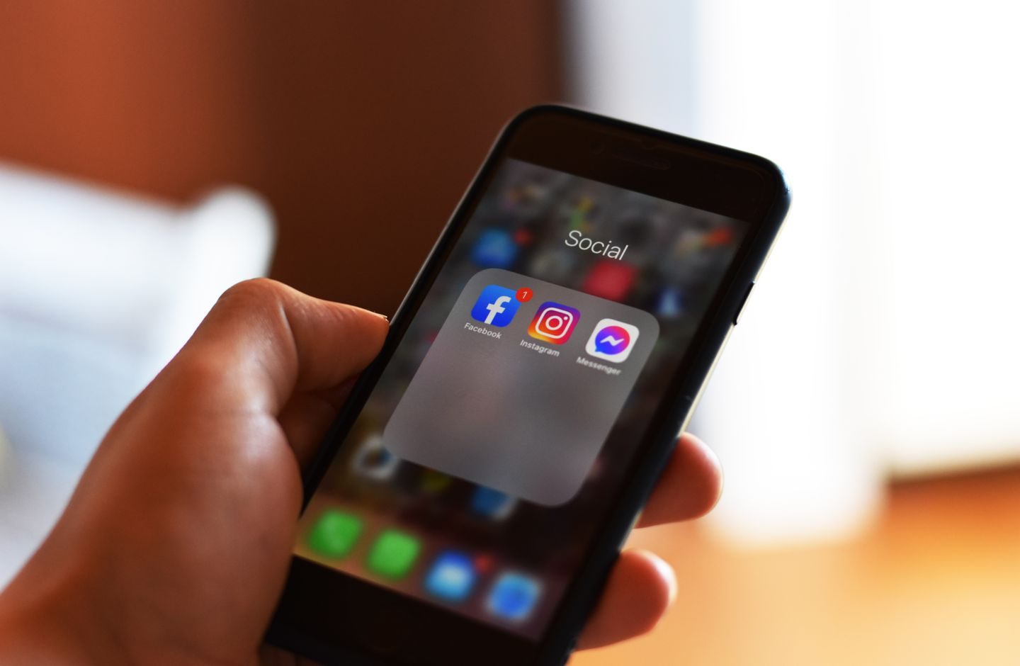 A hand holding a smartphone displaying app icons on the screen.