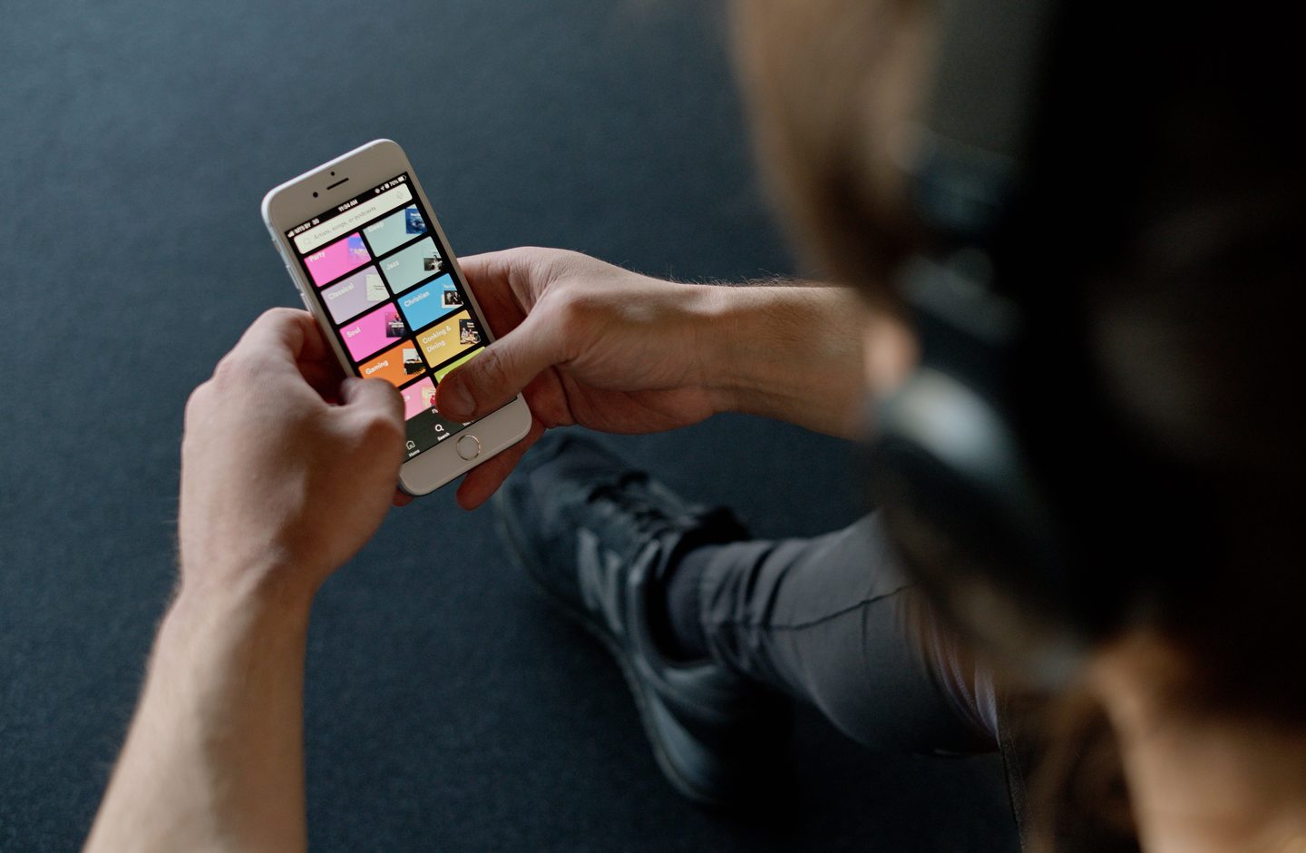 A person wearing headphones holding a smartphone, using an app with colorful category tiles.