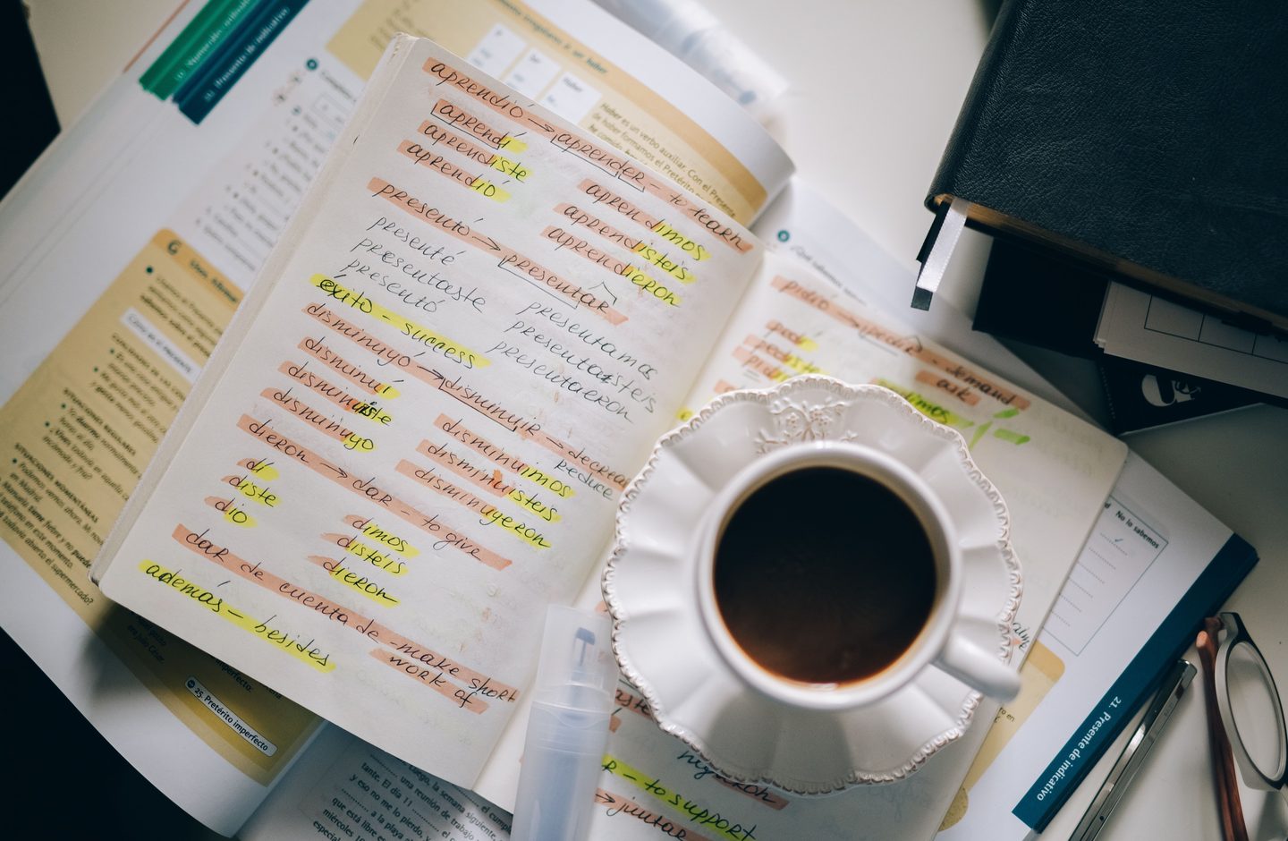 A notebook full of handwritten foreign-language vocabulary with translations, next to a cup of coffee.