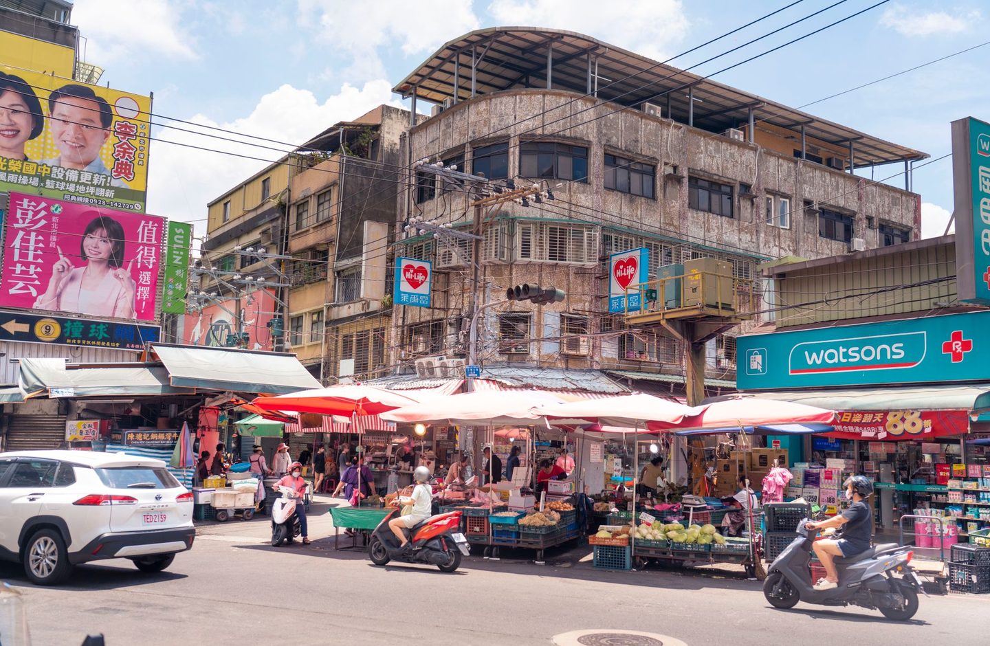 A bustling outdoor neighbourhood market in New Taipei City, Taiwan, with vendors, parked scooters and shop signage.