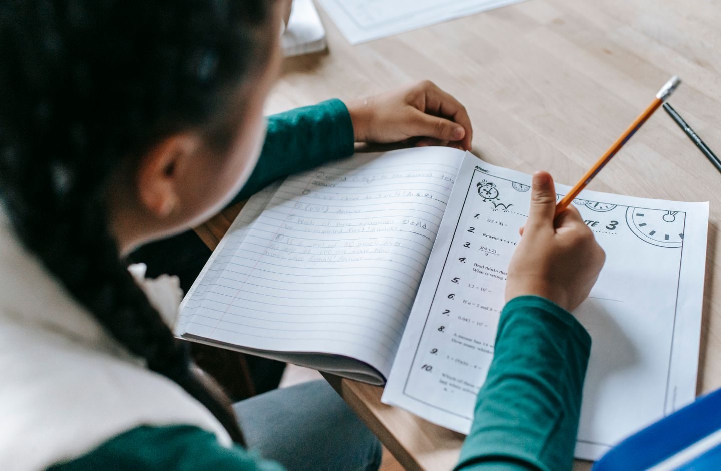 A student writing carefully in a notebook, pencil in hand.