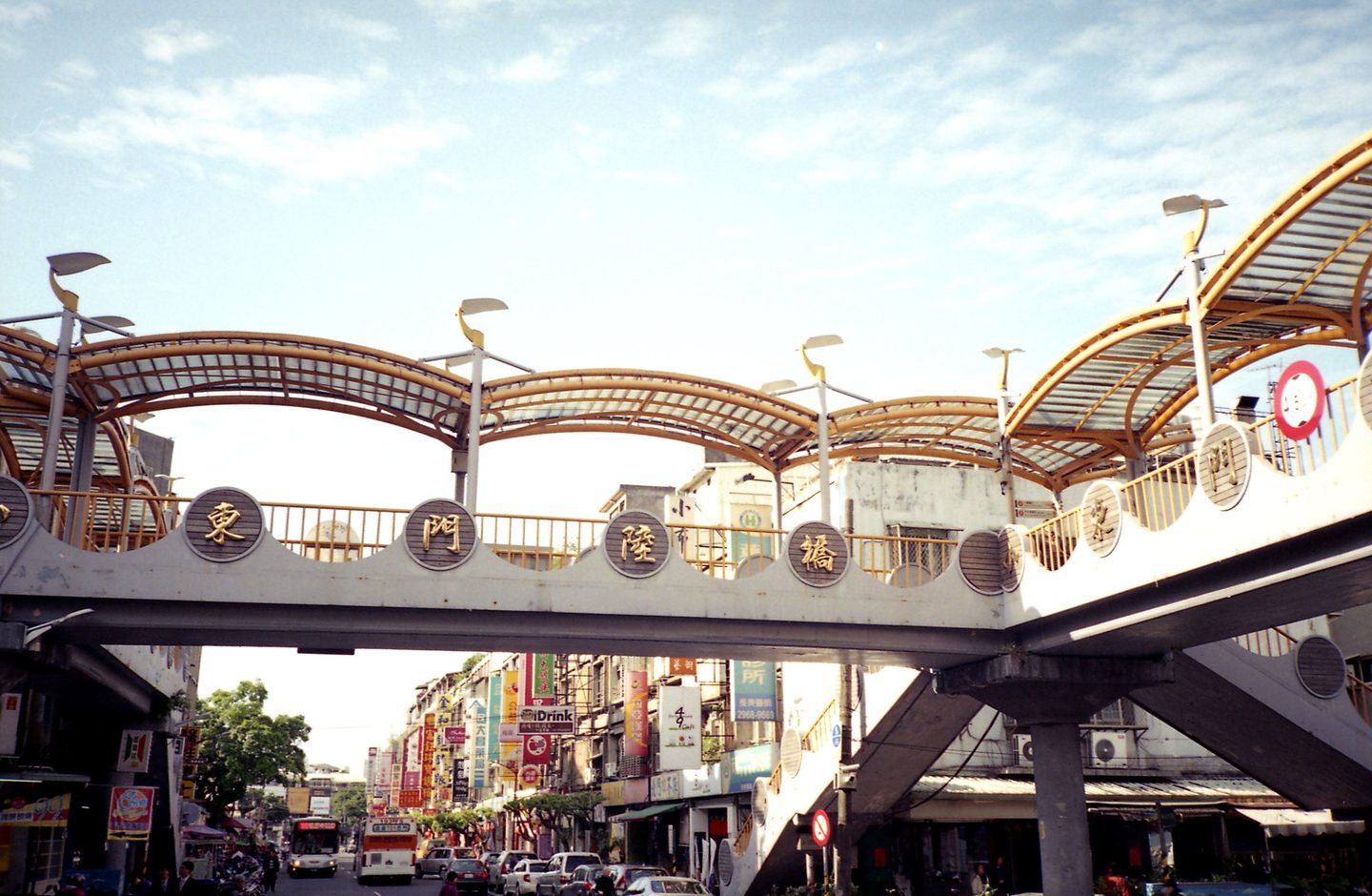 A pedestrian footbridge over a busy street in Tainan, Taiwan, with Traditional-character shop signs lining the road below.