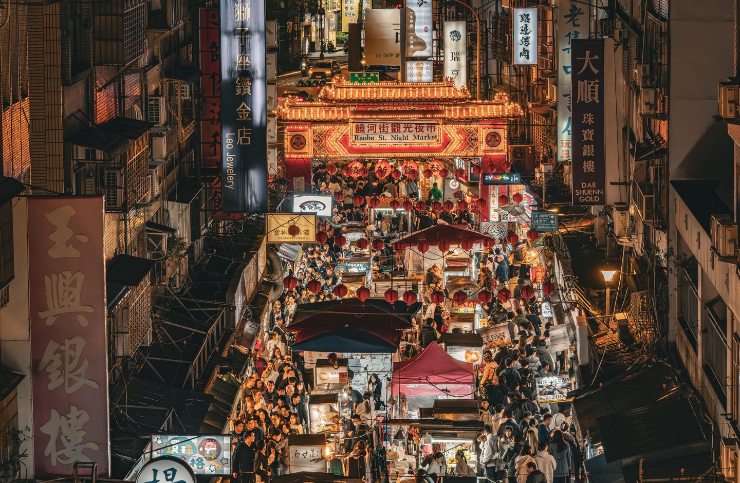 An aerial view of Raohe Street Night Market in Taipei, lit up at night with red lanterns and Traditional Chinese signage.