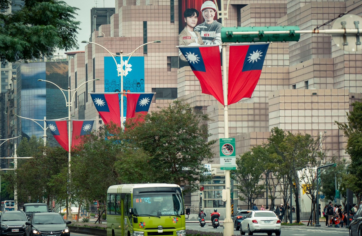 A Taipei street lined with Taiwan flags, a city bus, and traffic beneath tiled office buildings.