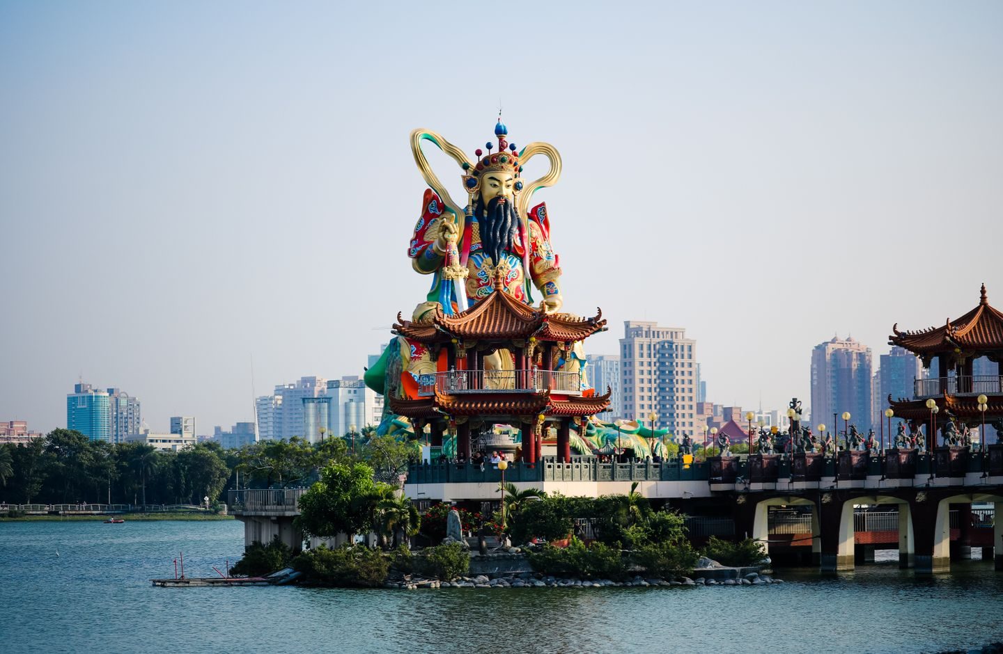 A large, colorful traditional temple statue on the water in Taiwan, with the city skyline behind it.