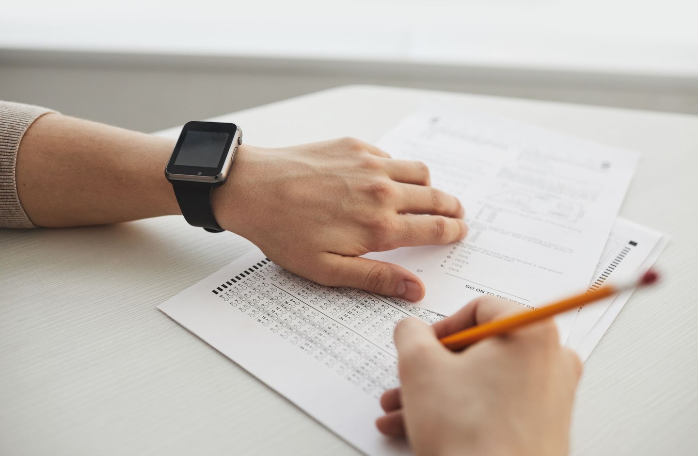 Close-up of a hand filling in a multiple-choice answer sheet with a pencil during a timed exam.