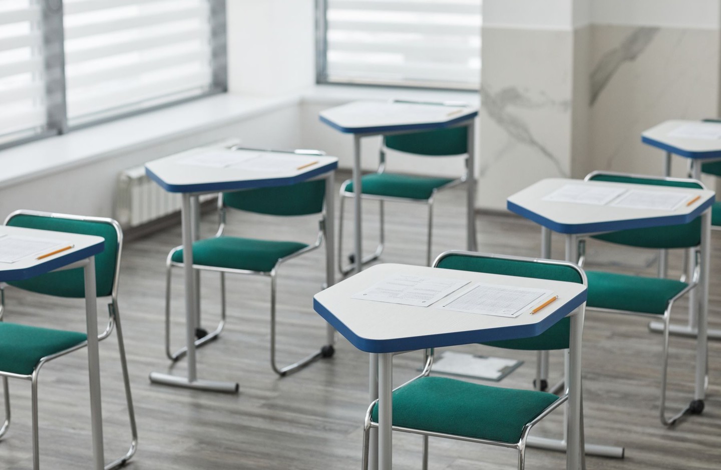 An empty exam room with individual desks, each holding a pencil and answer sheets, arranged for a formal test.