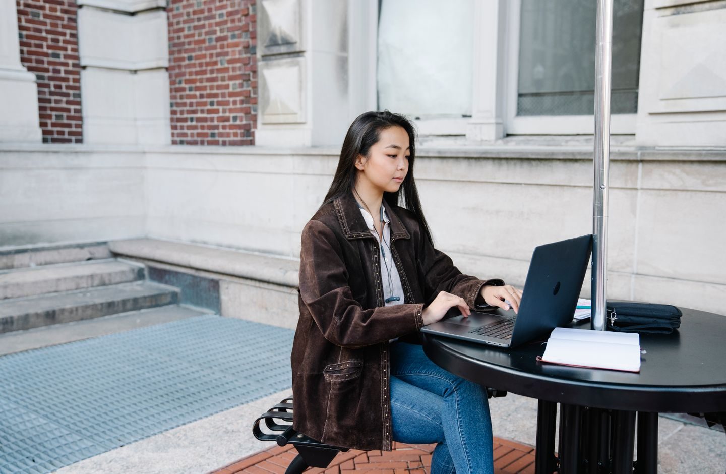 A woman sitting outdoors, focused on using a laptop.